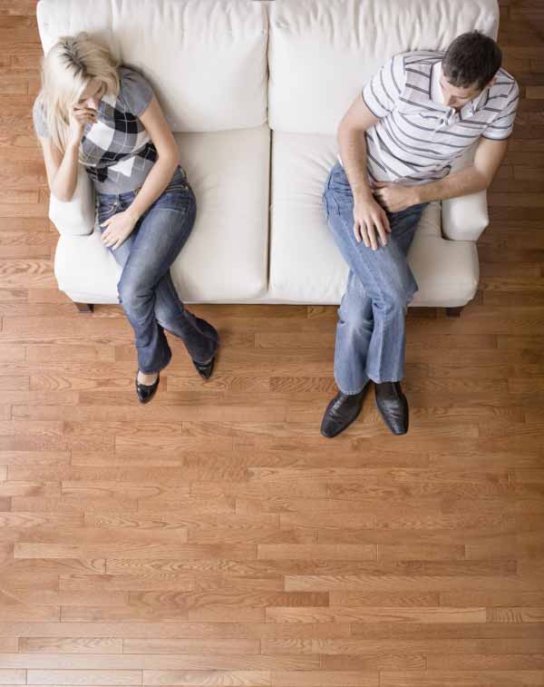 Man and a woman sit distantly on the ends of love seat.