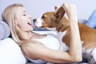 Beautiful young blonde woman playing with her dog at home