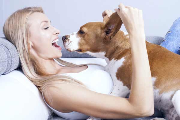 Beautiful young blonde woman playing with her dog at home