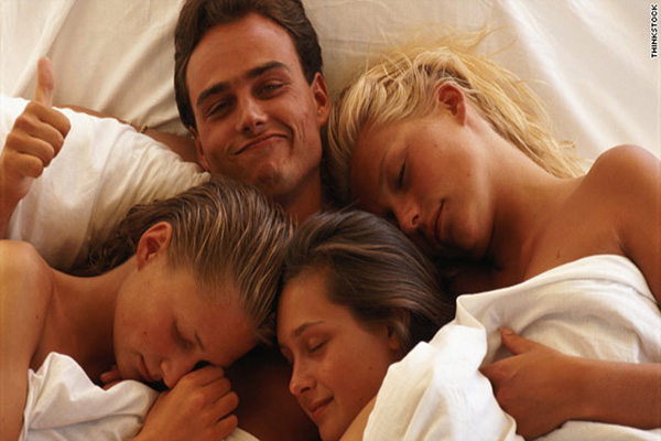 a happy man in bed surrounded by three girls